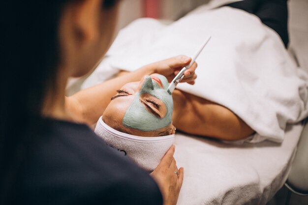 Cosmetologista aplicar máscara no rosto do cliente em um salão de beleza