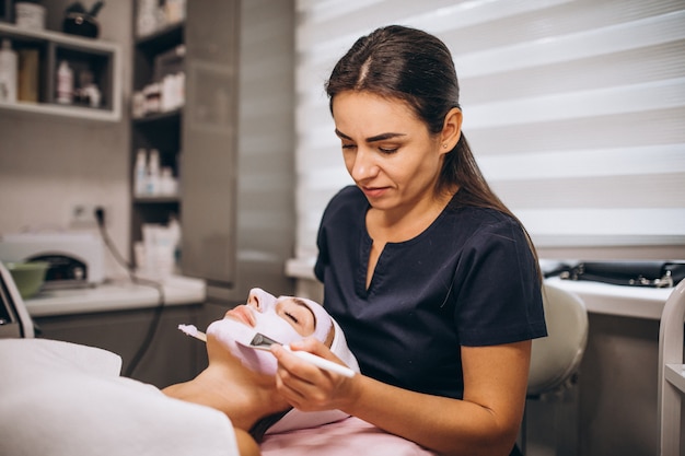 Cosmetologista aplicar máscara no rosto do cliente em um salão de beleza