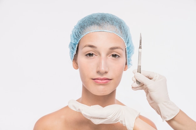 Cosmetologista segurando bisturi perto do rosto de mulher