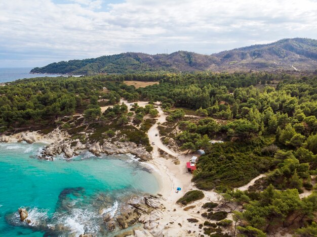 Costa do mar Egeu com água azul transparente, vegetação ao redor, pedras, arbustos e árvores, vista do drone, Grécia