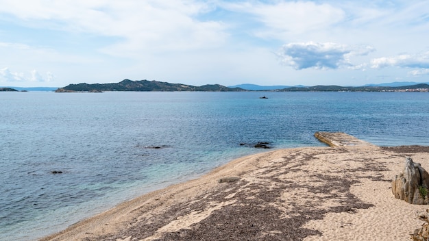 Costa do mar Egeu em Ouranoupolis com cais antigo e colinas verdes de uma ilha na Grécia