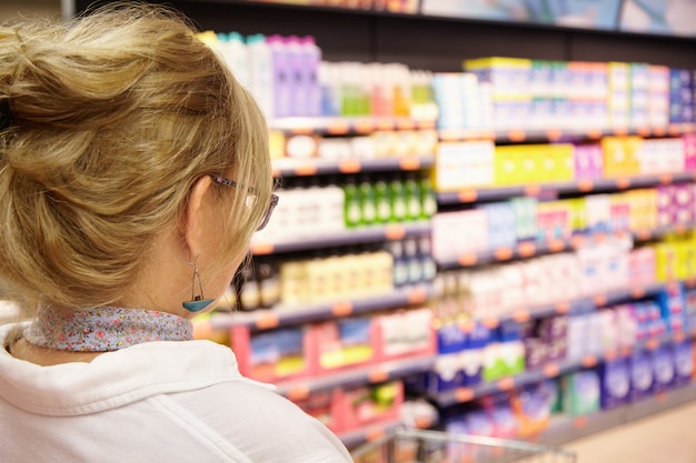 Costas tiro da avó com cabelo loiro, fazer compras no supermercado local, empurrando o carrinho para a frente, indo para a química doméstica