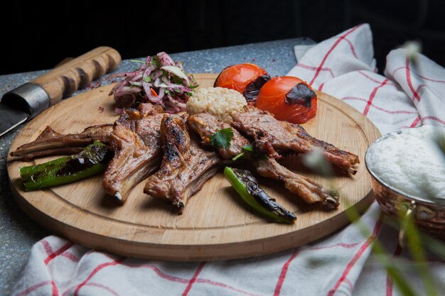 Costelas de kebab de vista lateral com legumes fritos e cebola picada e faca e ayran na bandeja de comida de madeira