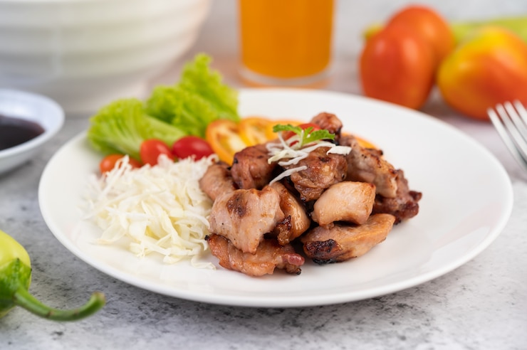 Foto grátis costeleta de porco grelhada com tomates e salada, dispostos em um prato branco.