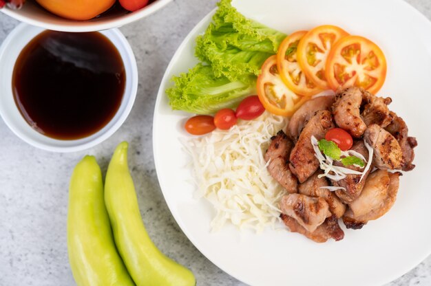 Costeleta de porco grelhada com tomates e salada, dispostos em um prato branco.