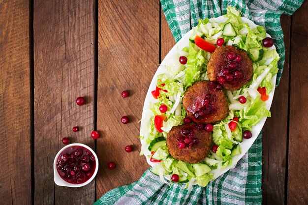 Costeletas de carne suculenta com molho de cranberry e salada em uma mesa de madeira em estilo rústico. Vista do topo