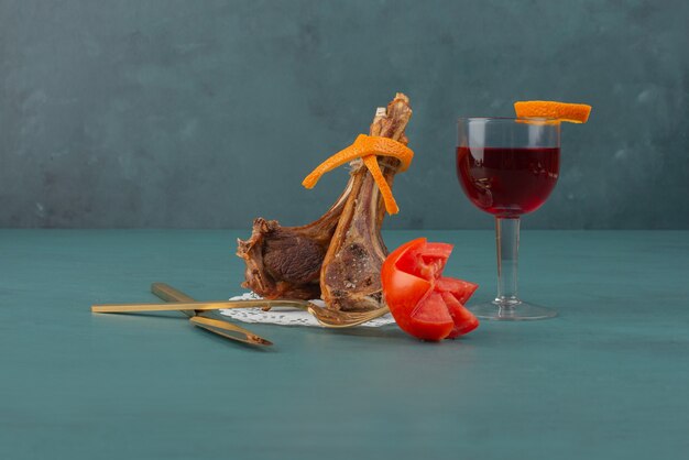 Costeletas de cordeiro grelhadas e um copo de suco na mesa azul.