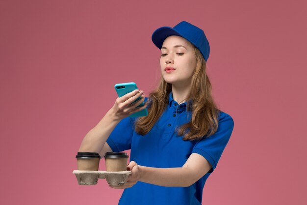 Courier feminina de uniforme azul tirando uma foto de entrega de xícaras de café em um uniforme de serviço de mesa de luz rosa