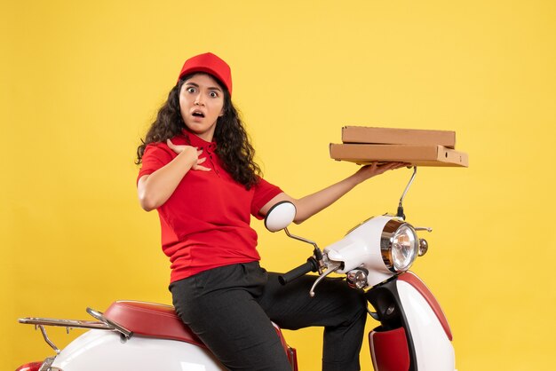 Courier feminino em bicicleta segurando caixas de pizza na mesa amarela.