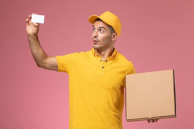 Courier masculino de uniforme amarelo segurando um cartão branco e uma caixa de entrega de comida rosa