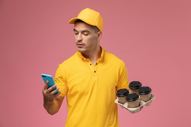 Courier masculino de uniforme amarelo segurando xícaras de café enquanto usa o telefone na mesa rosa