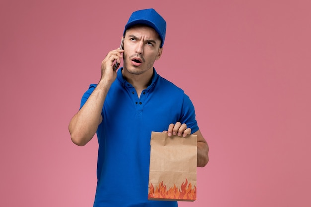 Courier masculino de uniforme azul falando ao telefone na parede rosa, entrega de serviço de trabalhador de trabalho uniforme