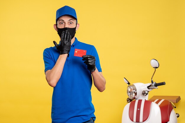 Courier masculino de uniforme azul segurando um cartão do banco no uniforme amarelo de serviço de emprego covid - pandemia de entrega de trabalho de vista frontal