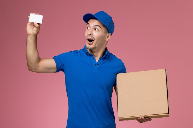 Courier masculino de uniforme azul segurando uma caixa de comida de cartão branco na parede rosa, entrega de serviço de uniforme de trabalhador