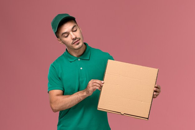 Courier masculino de uniforme verde segurando a caixa de comida na mesa rosa