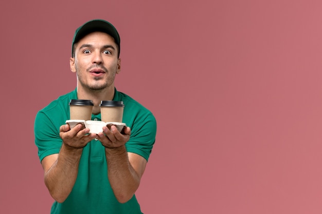 Foto grátis courier masculino de uniforme verde segurando xícaras de café marrom no fundo rosa