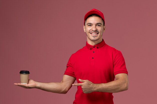 Courier masculino de uniforme vermelho segurando a xícara de café de entrega na mesa rosa trabalhador masculino