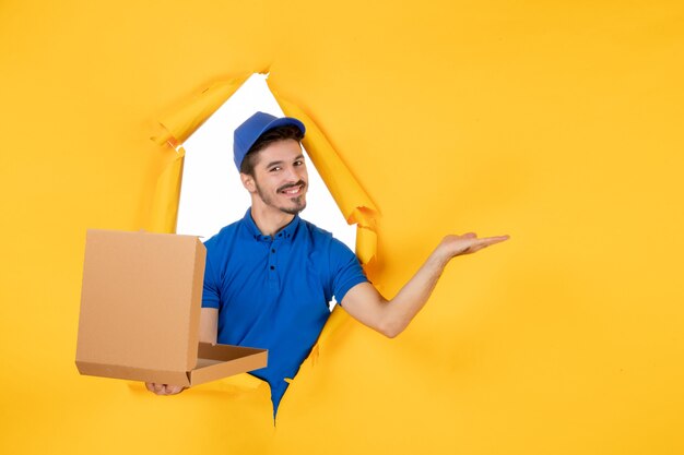 Courier masculino de vista frontal segurando uma caixa de pizza aberta e sorrindo no espaço amarelo