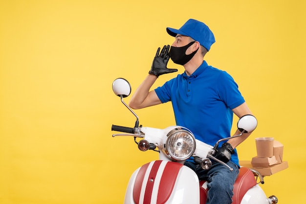 Courier masculino sentado em uma bicicleta, mascarado, chamando alguém no serviço de trabalho amarelo, pandemia, entrega, covid, uniforme, emprego