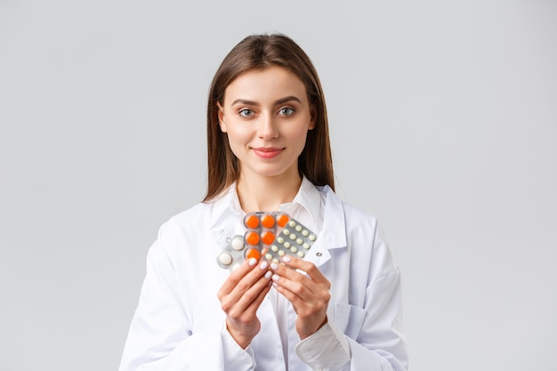 Foto grátis covid-19, prevenção de vírus, saúde, profissionais de saúde e conceito de quarentena. médico em jaleco branco médico, atraente médica mostrando remédios, pílulas diferentes, sorrindo enquanto recomendo