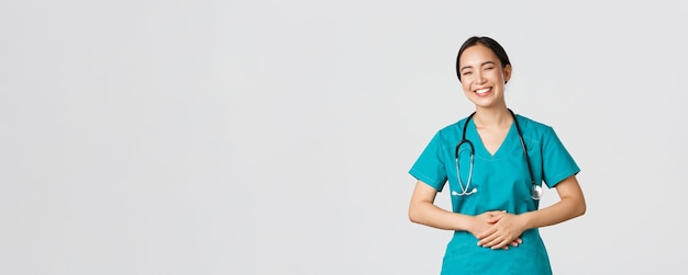 Covid-19, profissionais de saúde, conceito de pandemia. feliz médica muito asiática, médica de uniforme se divertindo, rindo e tocando a barriga enquanto brincava com a equipe do hospital.