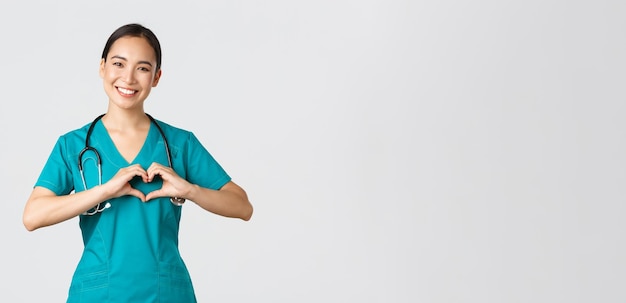 Covid-19, profissionais de saúde, conceito de pandemia. Linda carinhosa médica asiática, enfermeira feminina de esfrega, mostrando o gesto do coração e sorrindo, cuidando dos pacientes com amor, fundo branco.