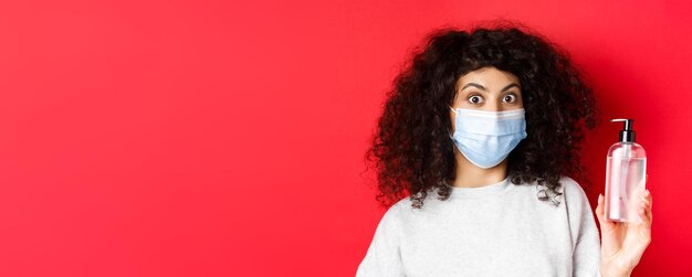 Foto grátis covid pandemia e conceito de quarentena animado garota com cabelo encaracolado usando máscara médica mostrando bott