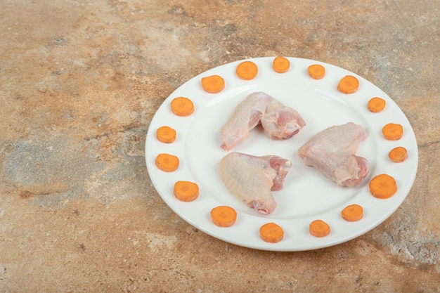Foto grátis coxa de frango cru com cenoura fatiada em prato branco