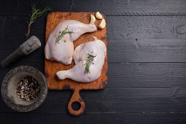 Coxas de frango cru na superfície de madeira escura.