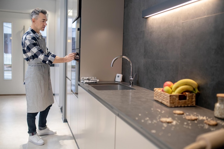 Foto grátis cozinhar em casa homem de meia-idade atento em roupas casuais tocando o painel de controle do forno na cozinha