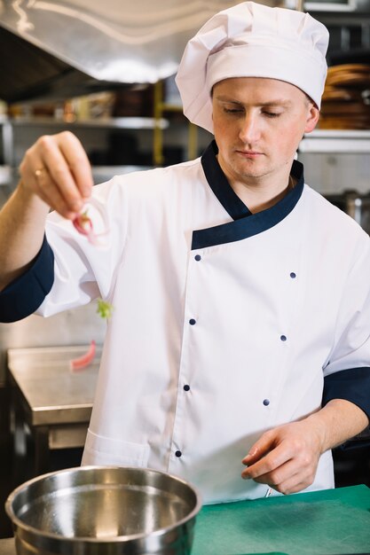 Cozinhe colocando legumes na tigela para salada