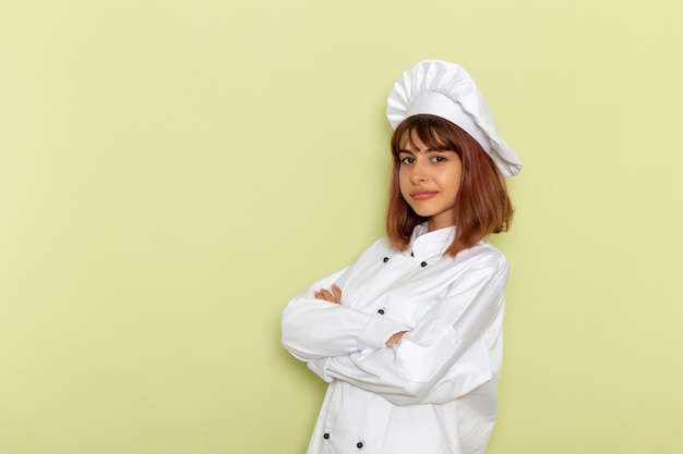 Cozinheira de frente para a cozinheira em um terno branco, posando e sorrindo na superfície verde