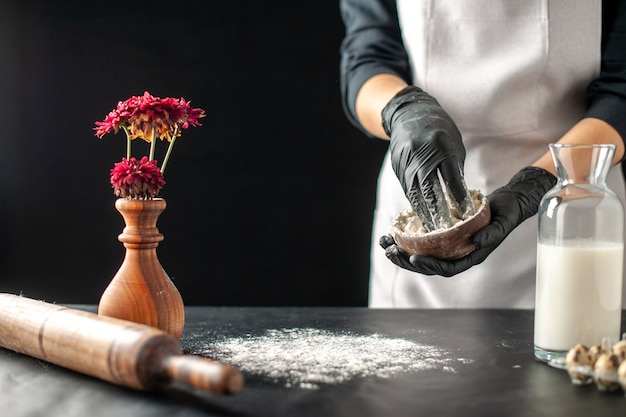 Cozinheira de frente, servindo farinha branca na mesa para a massa no trabalho de frutas escuras, pastelaria, torta, confeitaria, confeitaria