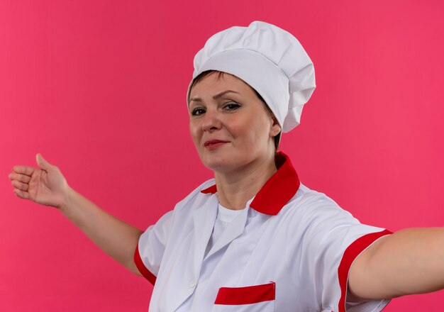 cozinheira de meia-idade com uniforme de chef mostrando o tamanho na parede rosa isolada