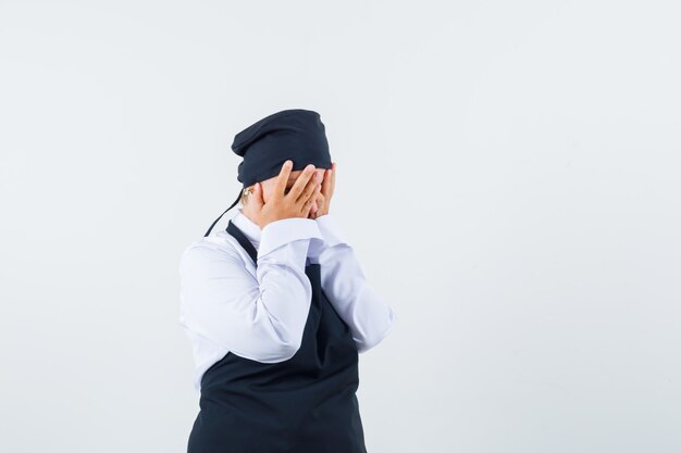 Cozinheira feminina de mãos dadas no rosto de uniforme, avental e parecendo deprimida. vista frontal.
