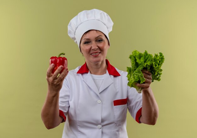 Cozinheira sorridente de meia-idade com uniforme de chef segurando salada e pimenta