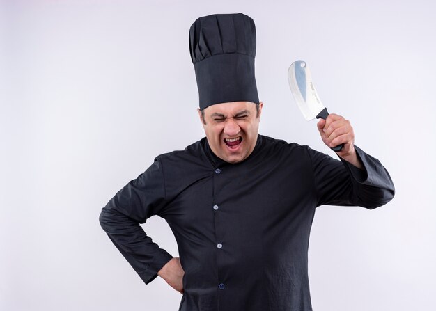 Cozinheiro chef louco louco vestindo uniforme preto e chapéu de cozinheiro balançando uma faca, gritando com uma cara de raiva em pé sobre um fundo branco