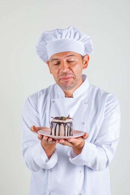 Cozinheiro chef masculino segurando o bolo com os olhos fechados em uniforme e chapéu