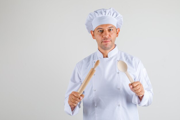 Cozinheiro chef masculino segurando o rolo e a colher de pau no chapéu e uniforme