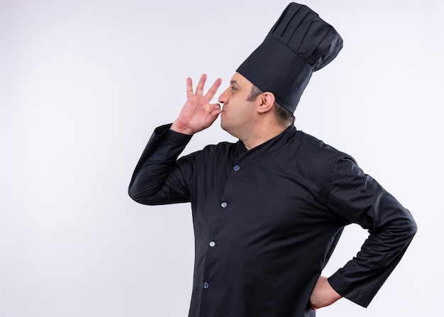 Foto grátis cozinheiro chef masculino usando uniforme preto e chapéu de cozinheiro, mostrando sinais de estar em pé delicioso sobre um fundo branco