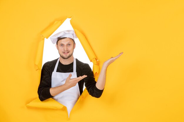 Cozinheiro de frente para o homem com capa branca e boné amarelo na cozinha rasgada foto colorida cozinha comida