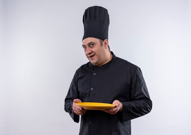 Cozinheiro de meia-idade impressionado com uniforme de chef segurando o prato na parede branca isolada
