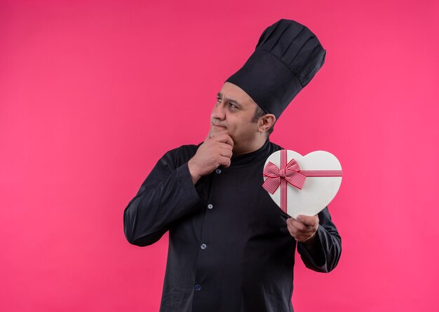 Cozinheiro de meia-idade pensando em uniforme de chef segurando uma caixa em formato de coração com espaço de cópia