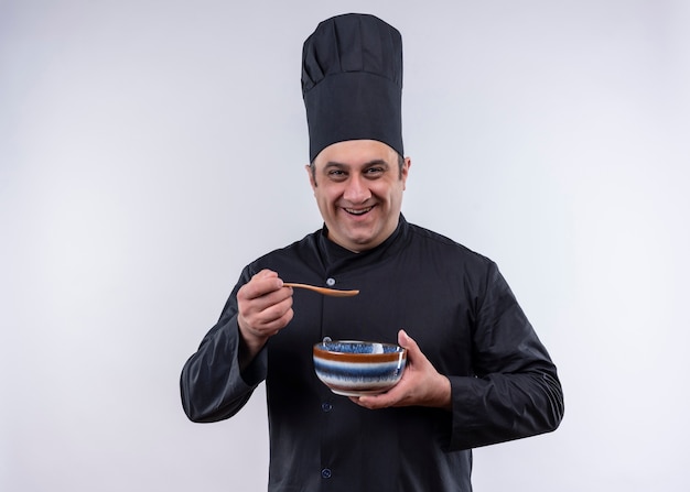 Cozinheiro de meia-idade sorridente com uniforme de chef segurando a tigela e a colher com espaço de cópia