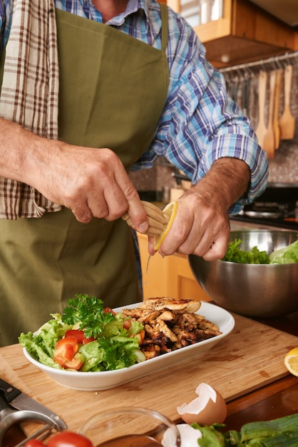 Cozinheiro masculino colhido adicionando suco de limão ao prato