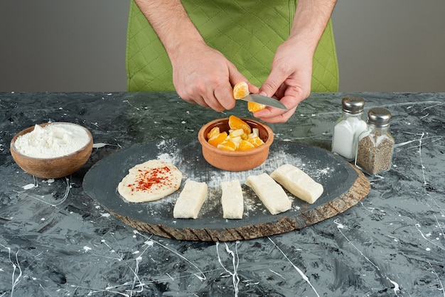 Cozinheiro masculino corta a laranja em pedaços na mesa de mármore.