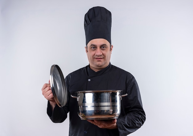 Cozinheiro masculino de meia-idade com uniforme de chef segurando uma panela e tampa na parede branca isolada