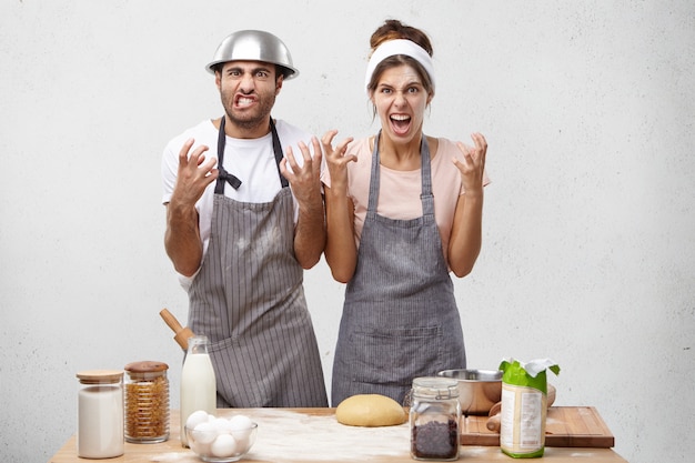 Cozinheiros femininos e masculinos irritados, mantêm as mãos em gesto de raiva, sendo irritados com o chef