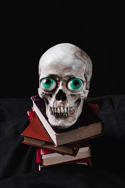 Crânio assustador com olhos de brinquedo engraçado na pilha de livros