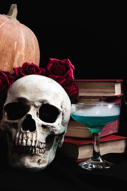 Crânio com bebida verde, livros e rosas